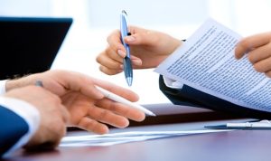 Business meeting at a table with two people, both holding pens and papers